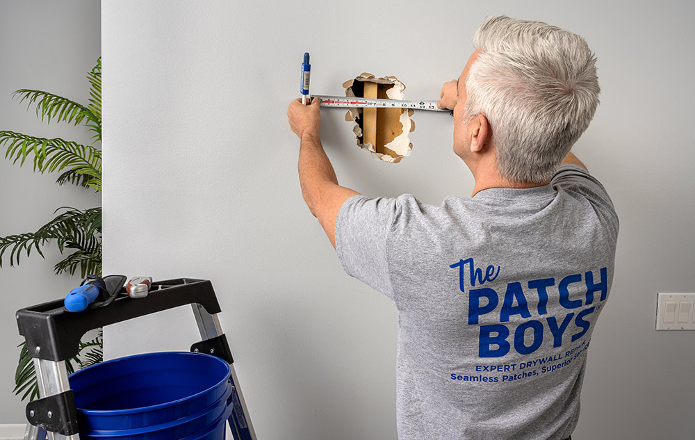Start a drywall repair business with THE PATCH BOYS franchise employee measures hole in the wall